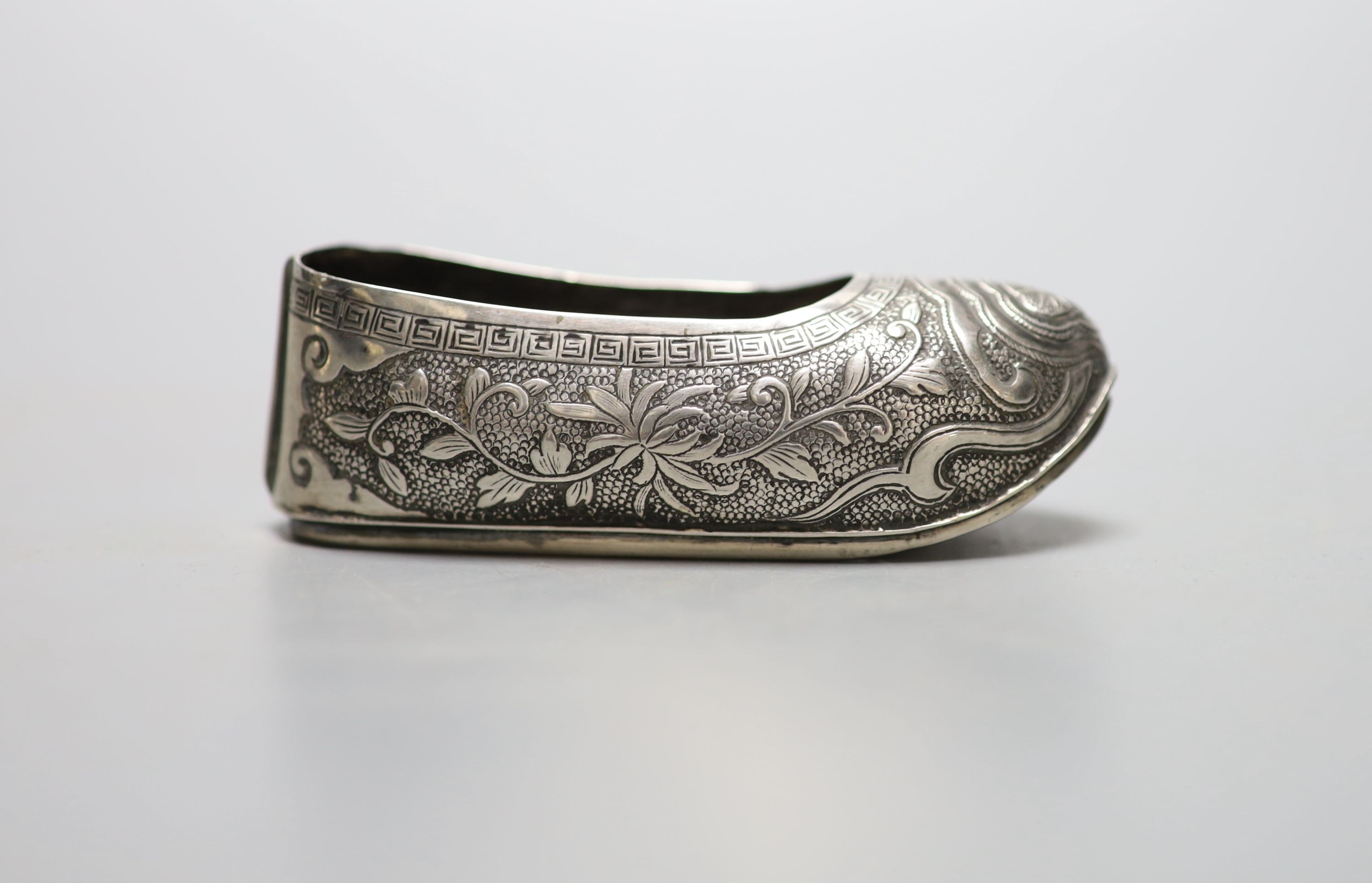 An early 20th century Chinese engraved white metal pin cushion, modelled a s a shoe, (lacking cushion), maker HC, 85mm.